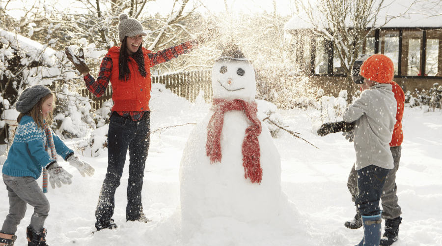 Kinder und junge Frau bauen gemeinsam einen Schneemann und freuen sich