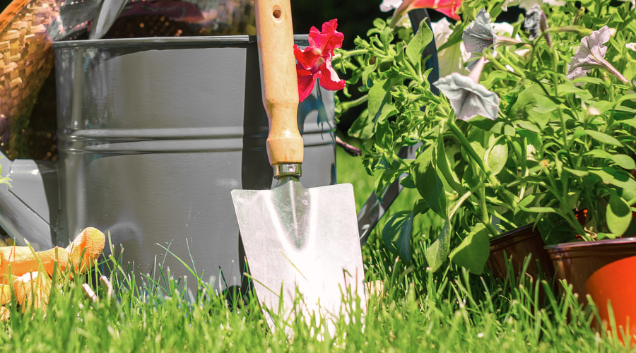 Gartengeräte für den Frühling: Schaufel, Hacke, Handgrubber und Gartenschere auf einem Holztisch im Garten, bereit für den Einsatz.