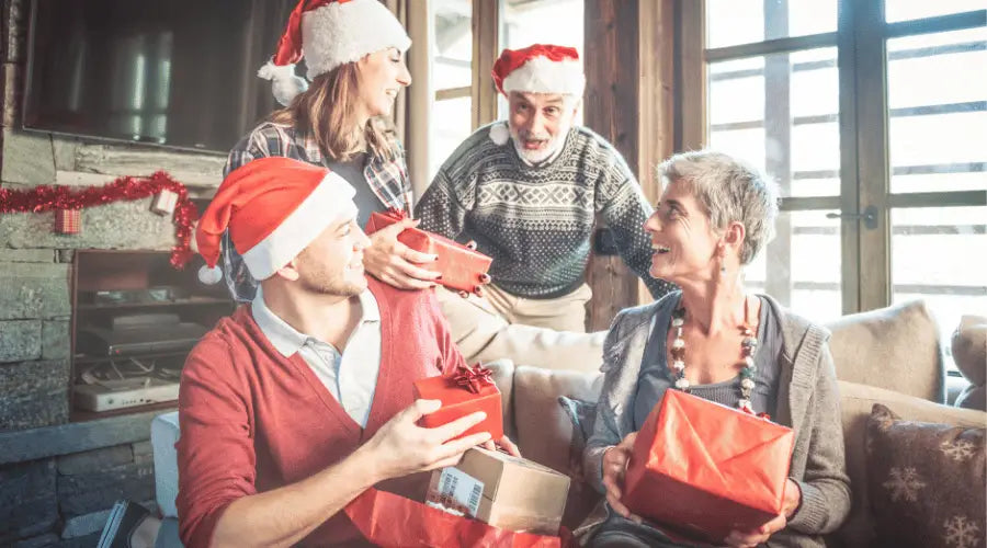 Mehrgenerationenfamilie bei der Weihnachtsbescherung im Wohnzimmer, voller Vorfreude und Emotionen, halten Geschenke in den Händen.