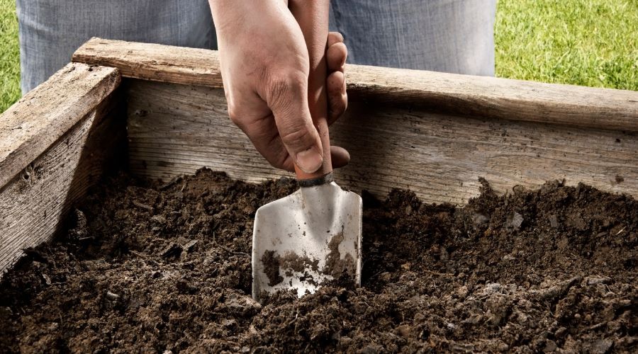 Hände beim Auflockern der Erde im Hochbeet mit einer Handschaufel – Vorbereitung zur Bepflanzung im Garten.