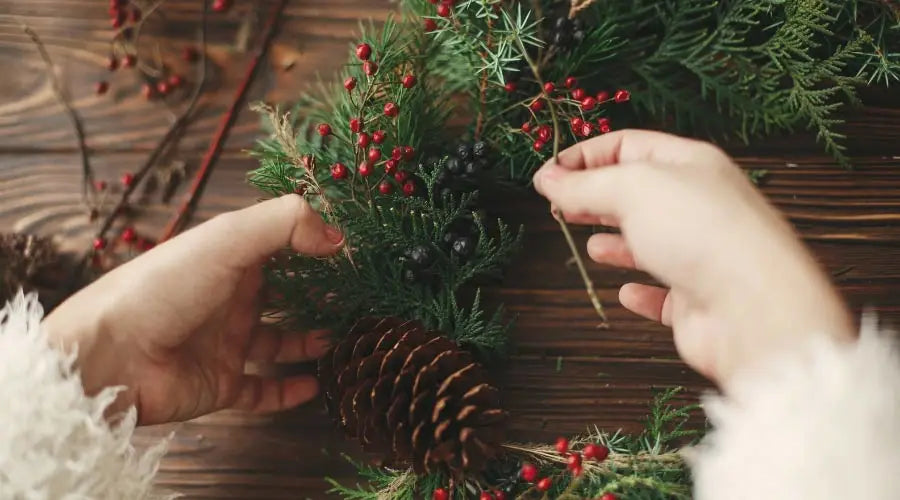 Frau bindet einen Weihnachtskranz mit Tannenzweigen und Beere
