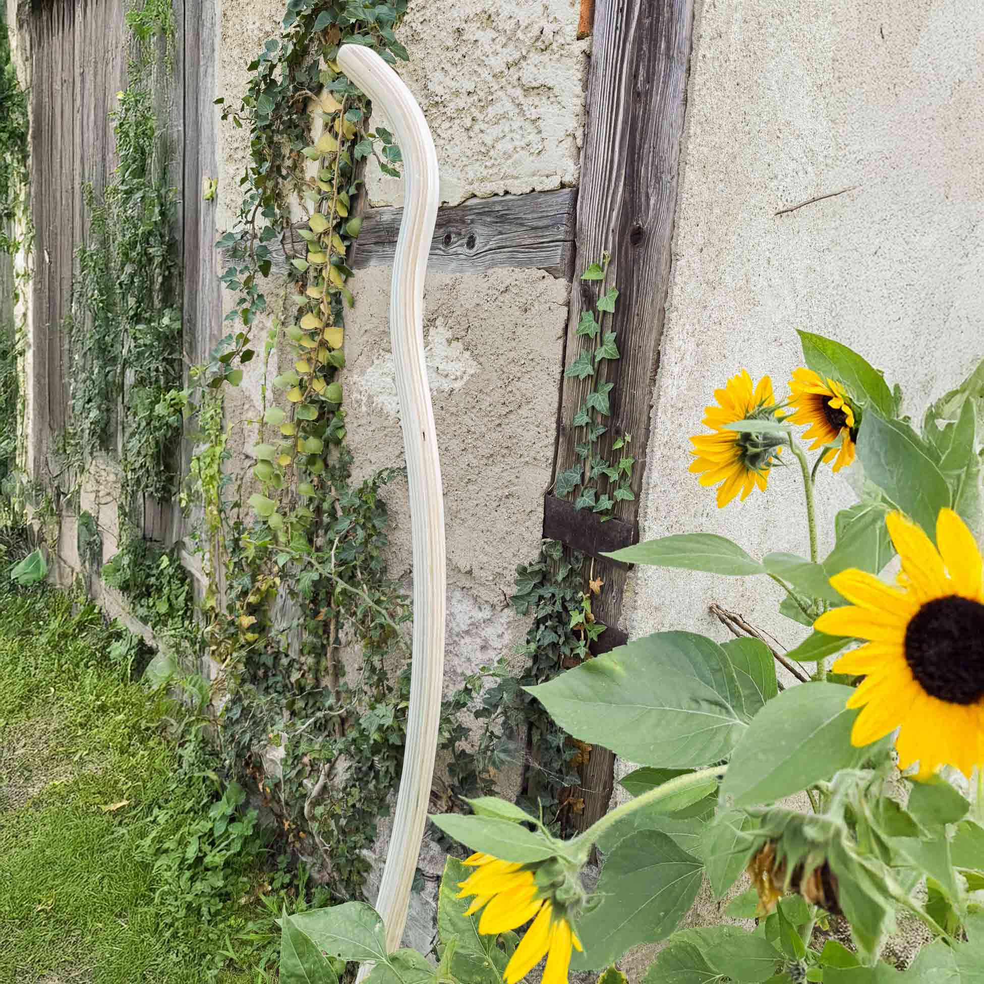 Ergonomisch gebogener Holzstiel für Gartengeräte von SHW vor Fachwerkhaus mit blühenden Sonnenblumen – hochwertiges Zubehör für ergonomische Gartenarbeit