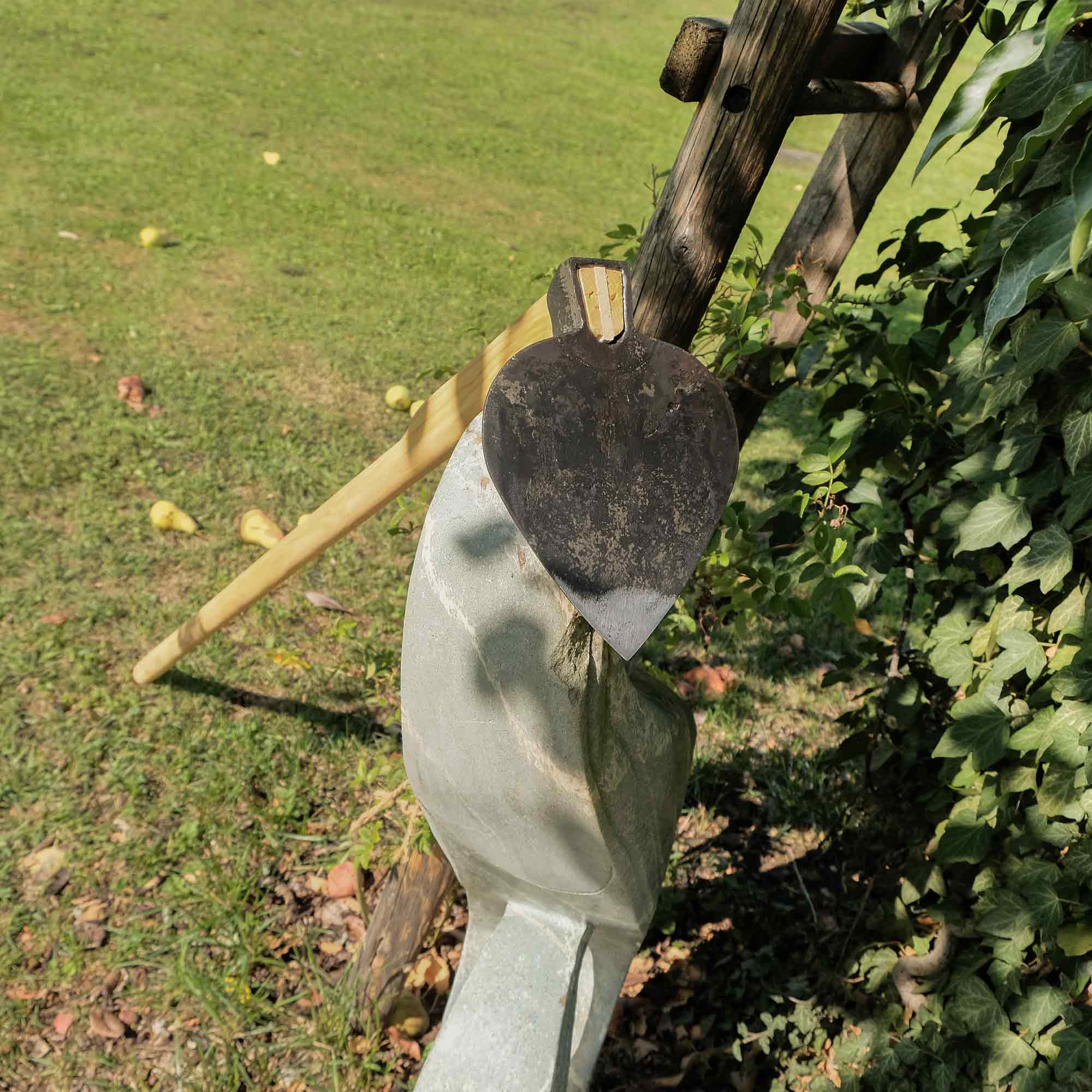 Herzform-Hacke mit Holzstiel an einer Gartenfigur angelehnt im Obstgarten