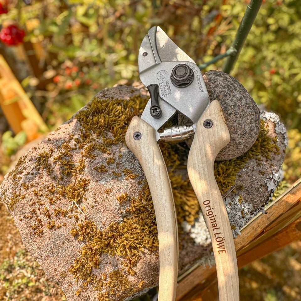 LÖWE Original 7 Natural Gartenschere mit ergonomischen Holzgriffen und robustem Metallkopf auf einem moosbewachsenen Naturstein im Garten.