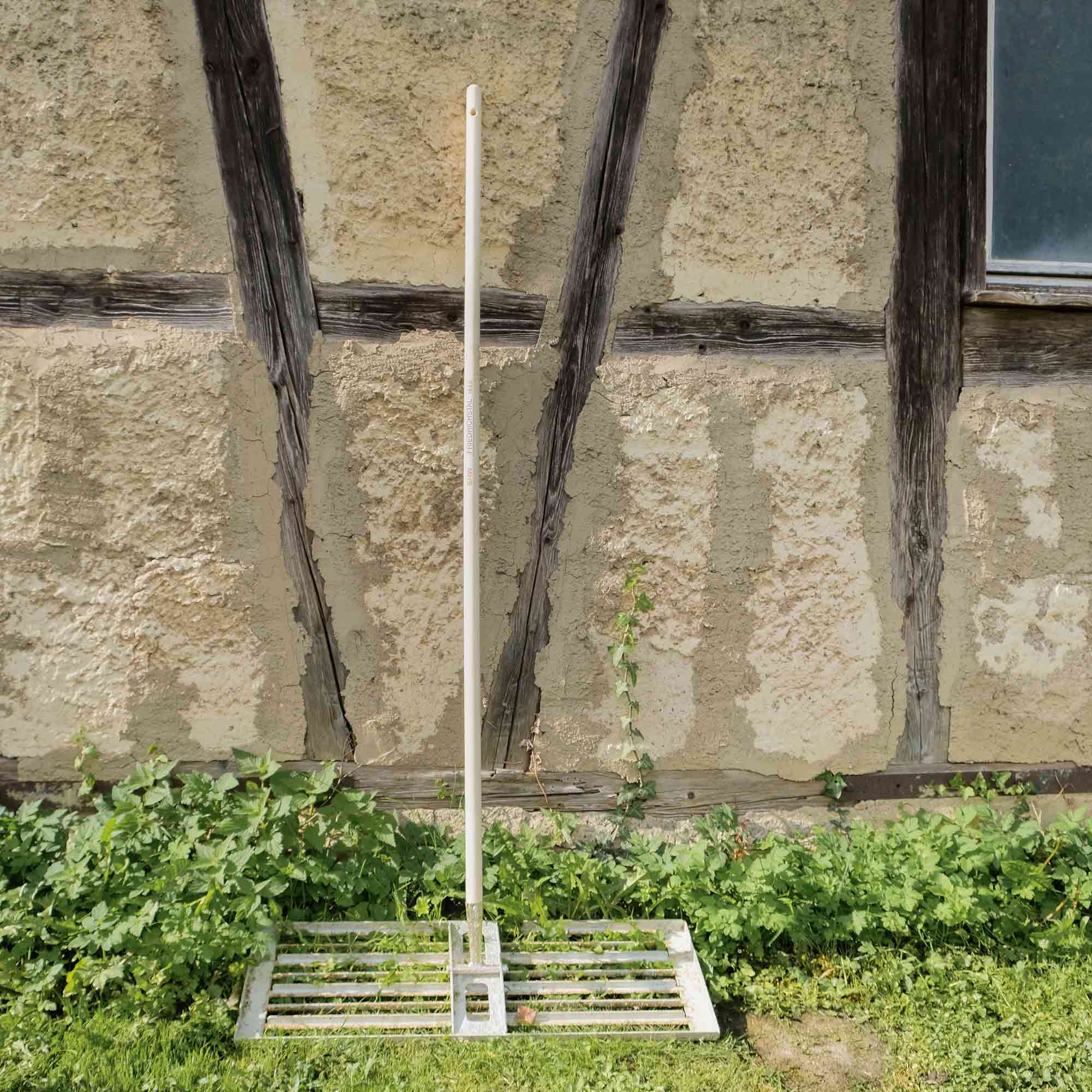 Rechen aus Metall mit langem Holzstiel vor rustikaler Fachwerkfassade