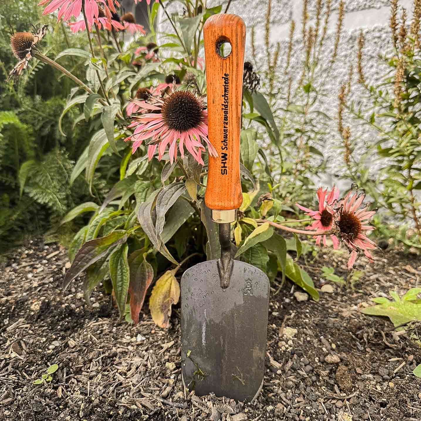 Pflanzkelle mit Holzgriff von SHW Schmiedetechnik im Blumenbeet vor blühendem Sonnenhut