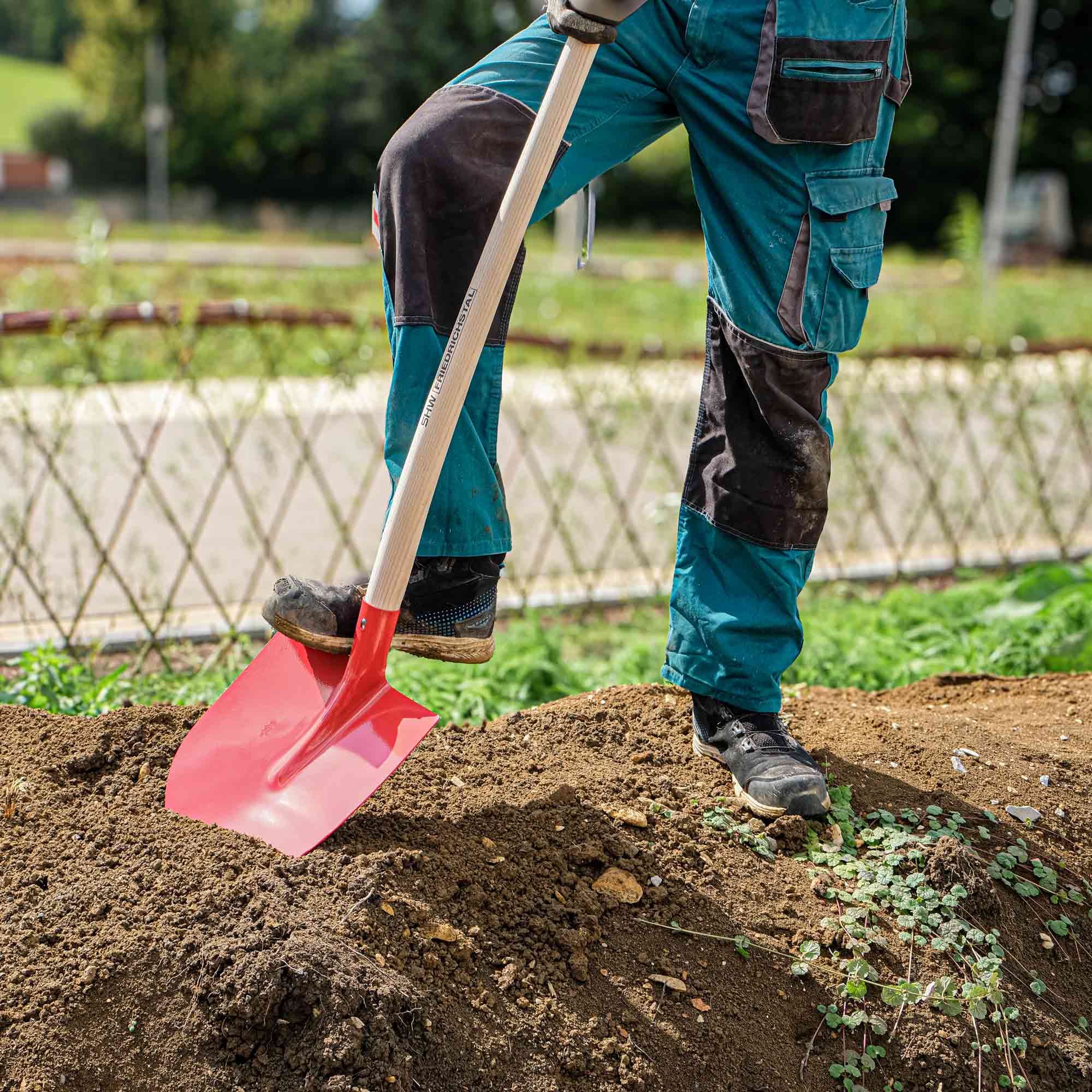 Gärtner sticht mit roter Schaufel und Holzstiel in den Boden eines Gemüsebeets