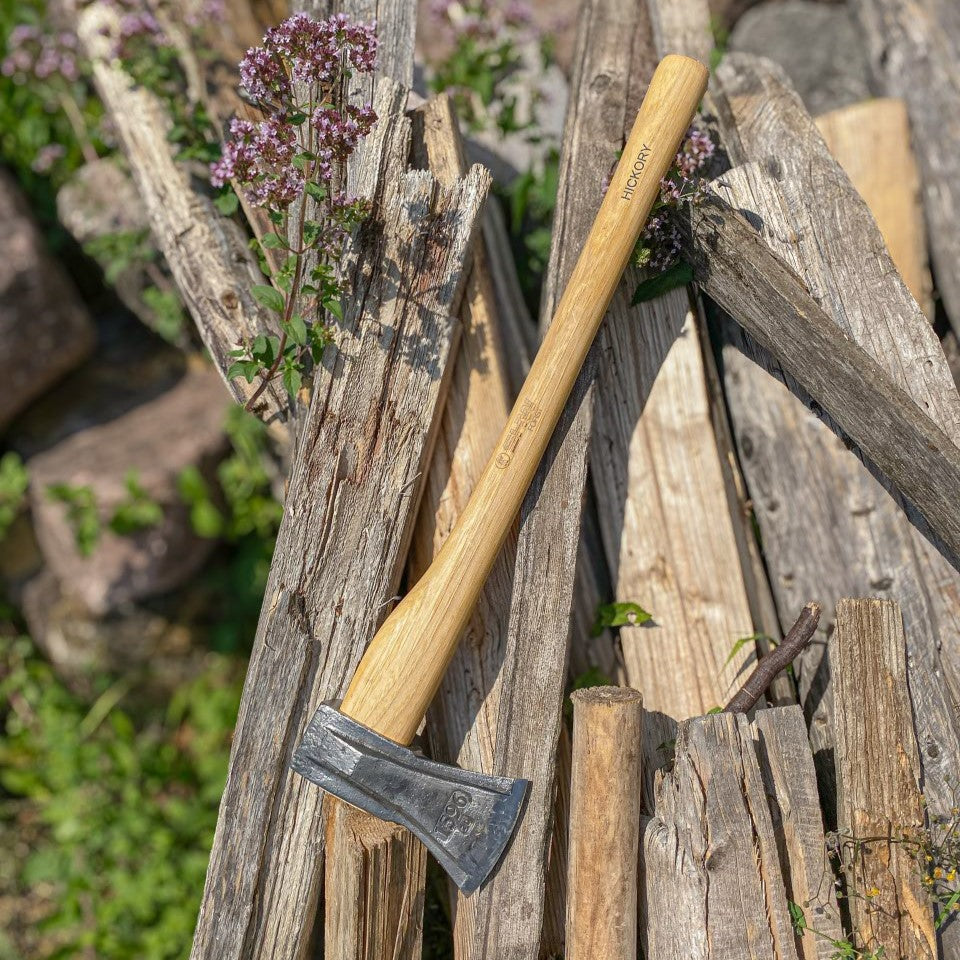 SHW Spaltaxt mit langem Hickorystiel und geschmiedetem Stahlkopf, angelehnt an einen Stapel gespaltenes Holz im Garten. Stabile Spaltaxt zur Herstellung von Brennholz.